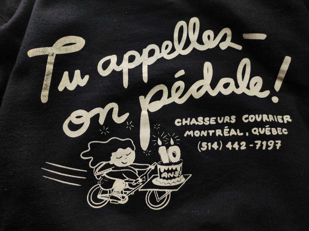 back of hoodie – same girl on cargo bike with cake with large cursive lettering that reads tu appeles - on pédale (you call, we pedal) and contact info for the company.